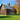 Rustic barn with weathered wood planks and a metal roof surrounded by green grass and autumn trees under a clear sky